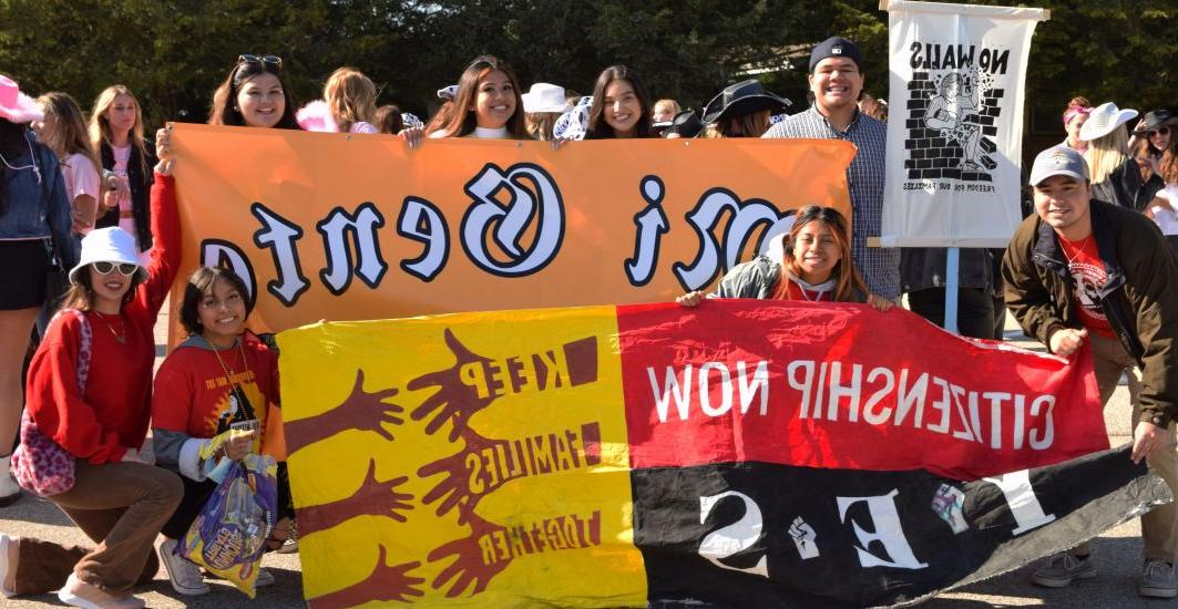 学生组织Mi Gente的学生在2021年返校节游行中举着横幅和标语. 